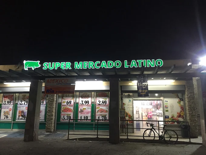 Fachada de Super Mercado Latino de noche, con el letrero verde iluminado